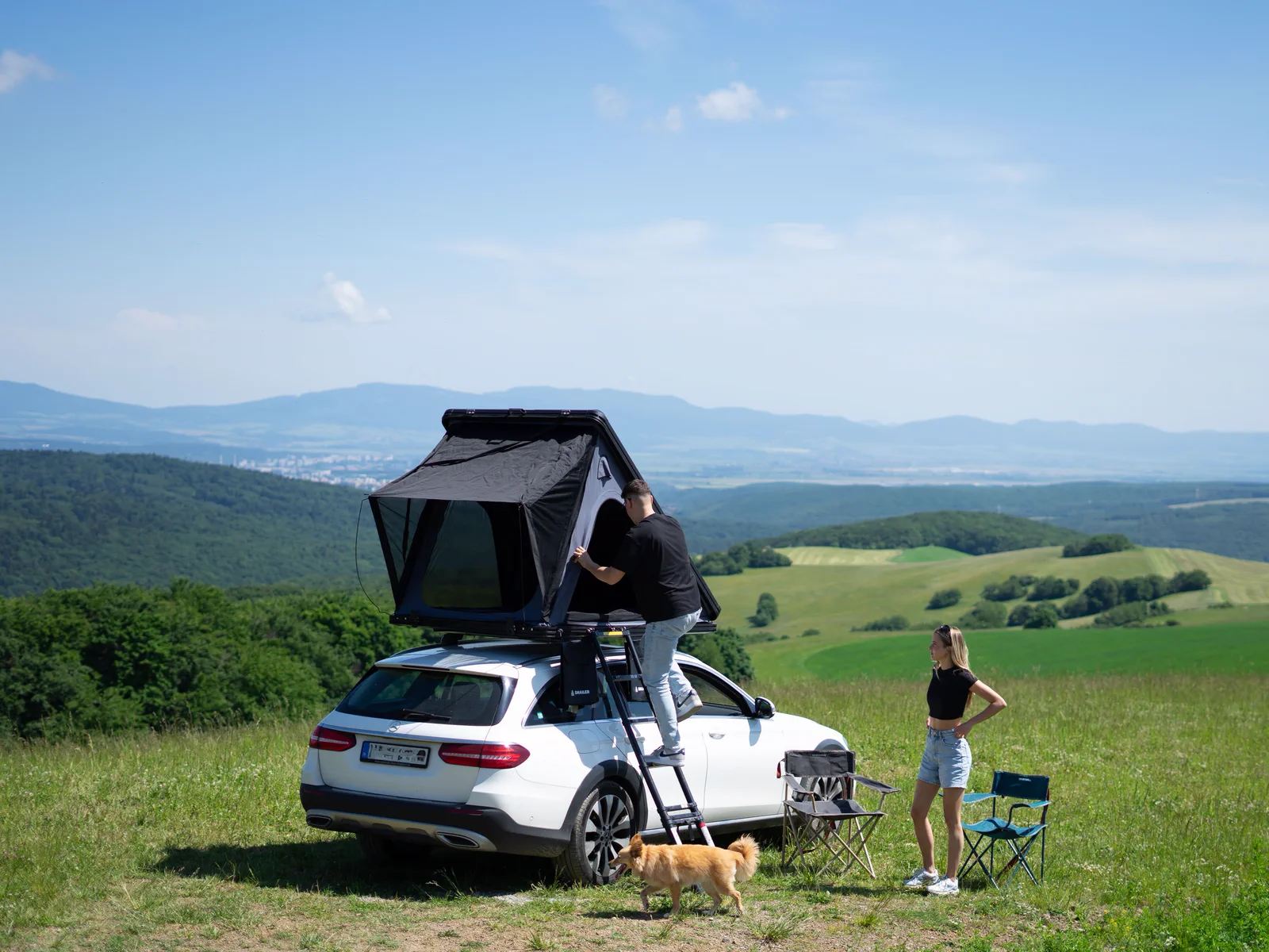 Pareja montando una tienda de techo SNAILER sobre un coche en una pradera de montaña